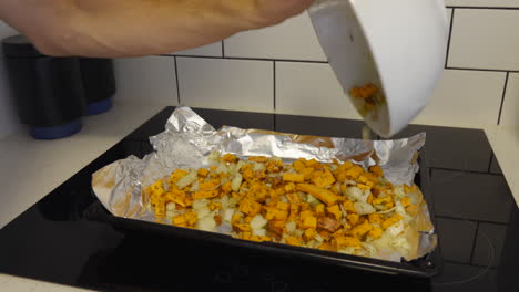 Die-Hand-Des-Mannes-Verteilt-Süßkartoffeln-Auf-Einem-Mit-Alufolie-Bedeckten-Tablett-Aus-Einer-Großen-Schüssel