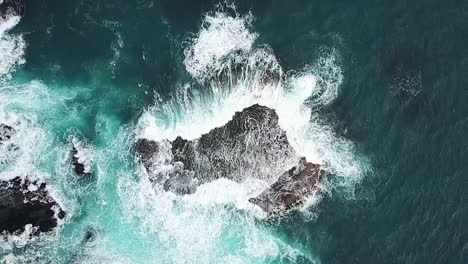 Slow-motion-aerial-of-waves-surging-over-rock-shelf-in-deep-aqua-blue-ocean