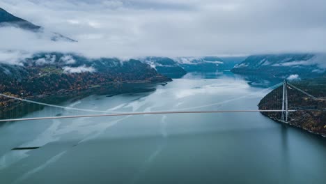 The-suspension-bridge-spanning-above-the-calm-blue-water-of-the-Eidfjorden-branch-of-Hardangerfjorden,-connecting-Ullensvang-and-Ulvik-regions