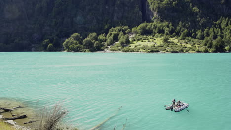 Two-fishermen-fish-on-a-boat-floating-on-turquoise-lake-with-the-view-of-steep-mountain-in-the-daytime