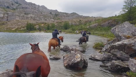 Männer-Zu-Pferd-Führen-Andere-Pferde-Entlang-Eines-Flusses