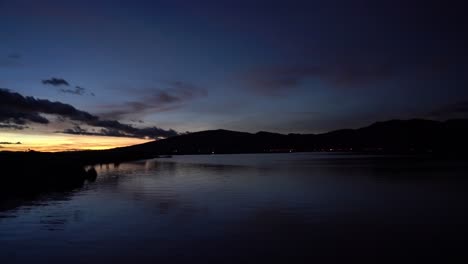 Ruhiger-Meerblick-Sonnenuntergang-Mit-Silhouette-Der-Berge-Im-Hintergrund-Mit-Dunkelblauem-Himmel