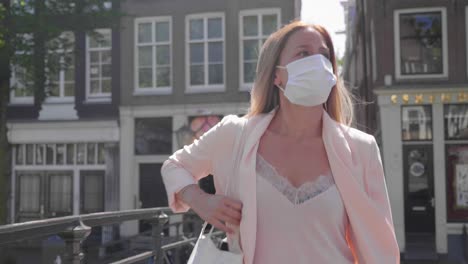 Brunette-Woman-With-Protective-Mask-Walking-On-The-Empty-Bridge-Across-Amsterdam-Canal---Coronavirus-In-Netherlands---medium-shot,-slow-motion
