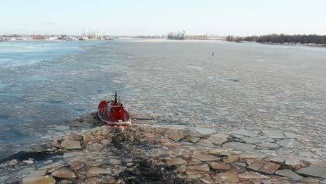 Aerial-view-follows-small-red-ship-sailing-along-drifting-ice-floes-creating-small-ripple-waves