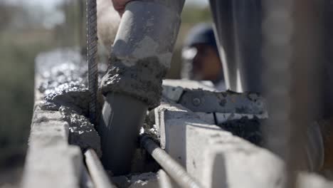 Construction-worker-pouring-wet-concrete-from-pipe-into-wall-formwork,-close-up
