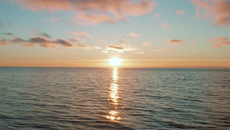 Drone-flying-over-calm-wavy-sea-at-sunset,-sunrise