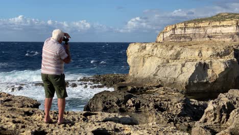 Unidentifiable-older-man-looks-through-camera-at-the-coast-of-Gozo,-Malta--Blue-Hole,-Dwejra