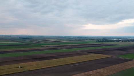 Aerial-shot-of-green,-yellow-and-brown-farm-fields-in-Europe-during-sunset