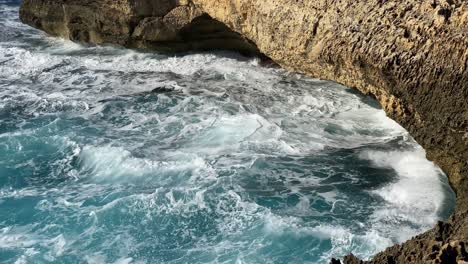 Choppy-sea-splashing-against-eroded-limestone-rock-face,-San-Lawrenz,-Gozo