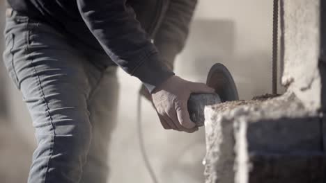 Laborer-on-dusty-construction-site-cutting-concrete-with-angle-grinder,-front-view