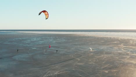 Beautiful-drone-shot-of-kite-boarding-over-frozen-sea-in-a-sunny-day