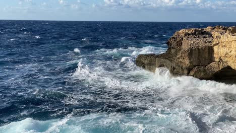 Tempestuous-waves-smash-agains-limestone-cliff-in-slow-motion,-sunny-afternoon-light