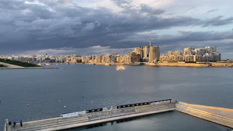 View-over-Valleta-United-Waterpolo-Pitch-of-sunlit-Sliema-skyline-under-rain-clouds