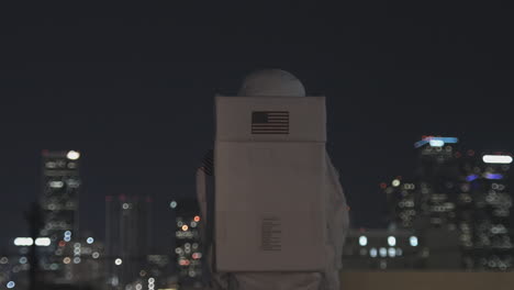 A-person-in-a-white-costume-with-an-american-flag-on-the-back-stands-and-looks-at-a-city-at-night