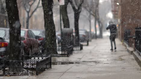 Man-stepping-out-onto-snowy-sidewalk-during-the-gentle-snowfall,-New-York-city---slow-mo-static-wide-shot