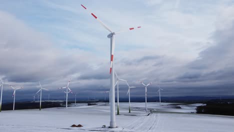 Luftaufnahme-Nach-Oben-Zu-Einem-Riesigen-Schneebedeckten-Windturbinenfeld,-Das-Im-Winter-Tagsüber-Saubere-Erneuerbare-Energie-Im-Freien-Erzeugt