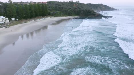 Aerial-backward-panning-shot-at-sunrise-along-beach-at-Port-Macquarie-with-unrecognisable-people