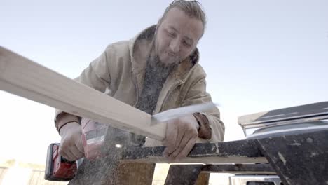 Young-caucasian-man-cutting-wood-with-reciprocating-saw,-slow-motion-low-angle
