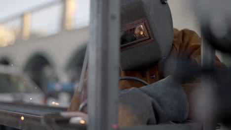 Welder-welding-metal-construction-in-workshop-sparks-shield-mask-slowmo