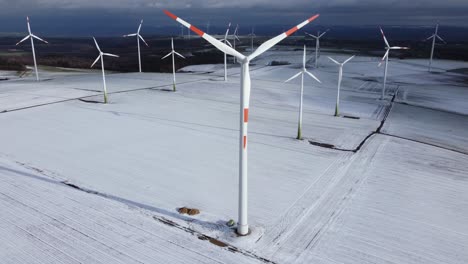 Aerial-tilt-up-shot-of-snowy-rural-fields-with-working-wind-turbine-farm-in-sunlight-during-iced-wintertime