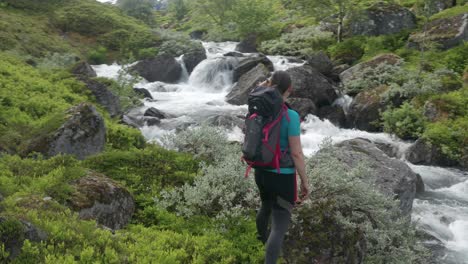 A-woman---hiker-with-a-backpack-standing-on-the-stone-near-a-powerful-and-noisy-water-stream