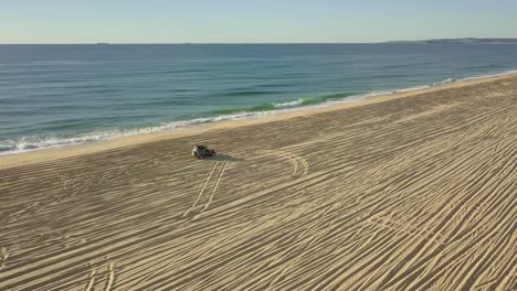 Aerial-view-of-a-4x4-car-driving-on-empty-beach-near-the-sea,-sideways-tracking