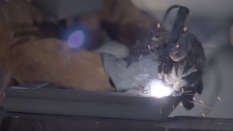 Sparks-fly-as-gloved-welder-fuses-angle-iron-together,-slow-mo-static-shot