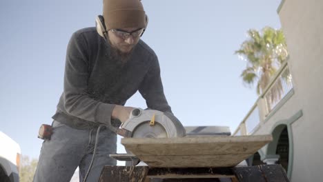 Carpenter-using-electric-circular-saw-outside-on-sunny-day,-low-angle-slow-motion