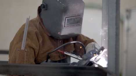 Welder-welding-metal-construction-in-workshop--sparks-shield-mask-circle-pan