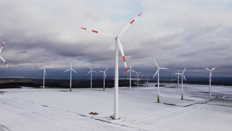 Aerial-trucking-shot-of-beautiful-ecological-wind-turbines-farm-for-green-energy-during-frosty-and-iced-winter-landscape-at-daytime