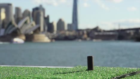 Nahaufnahme-Eines-Golfschlägers,-Der-Einen-Ball-In-Superzeitlupe-Mit-Sydney-City-Im-Hintergrund-Schlägt