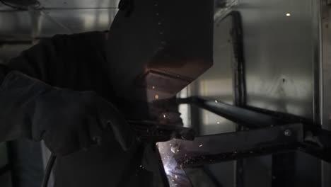 Sparks-fly-and-light-flickers-as-welder-fabricates-metal-frame--slow-mo,-truck-right
