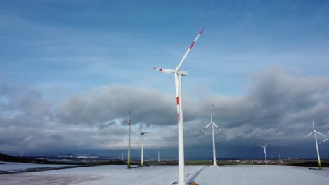 Low-angle-orbit-aerial-of-Electricity-Wind-Turbines-Farm,-Power-Clean-Alternative-Energy-with-winter-snow-during-sunny-day