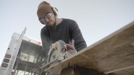 Low-angle-view-of-carpenter-cutting-wooden-board-with-electric-circular-saw