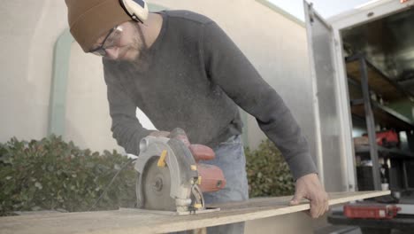 Carpenter-wearing-PPE,-ear-muffs-and-safety-glasses,-cuts-wood-with-circular-saw