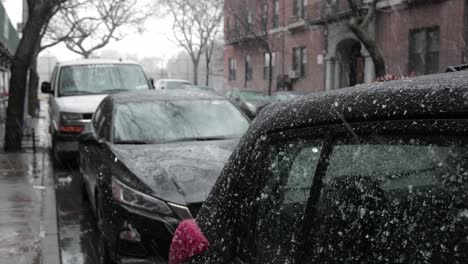 Gentle-snowfall-tumbling-down-and-covering-line-of-cars-parked-on-the-side-of-a-road-in-Brooklyn,-New-York---Medium-static-shot
