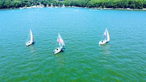 Rotating-aerial-view-of-sailboats-with-American-flag-at-Wallenpaupack-lake,-Pennsylvania,-USA