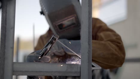 Welder-uses-arc-welder-to-tack-together-sections-of-angle-iron--slow-mo-dolly-back