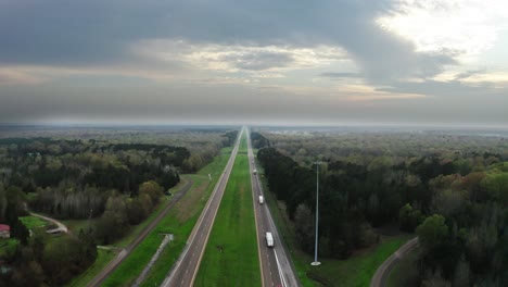 American-highway-with-green-forest-and-majestic-cloudy-sky-in-aerial