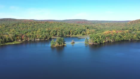 Fly-towards-small-lake-island-in-Harriman-State-Park-with-blue-water