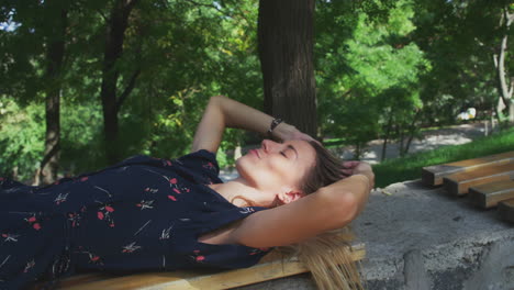 Young-Woman-Relaxing-Lying-Down-on-Park-Bench-in-Shade-of-Sun-Stretches-Arms-and-Opens-Eyes