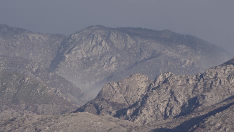 Mist-blowing-over-sunlit-mountain-range,-static-telephoto-shot