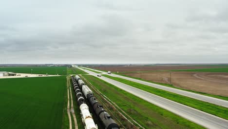 Railroad-with-train-near-highway-in-green-fields