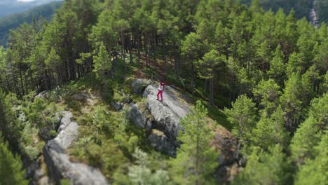 A-hiker-with-a-heavy-backpack-on-her-back-standing-on-the-rocky-outcrop-in-the-middle-of-the-forest-covered-plateau,-enjoying-the-view-of-the-vast-valley