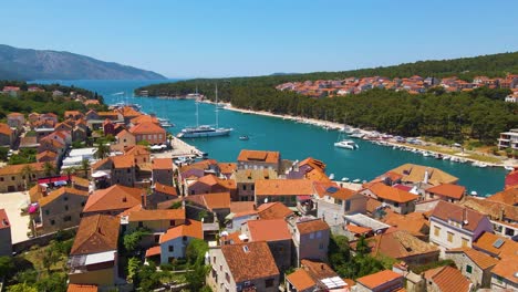 View-of-a-coastal-town-with-many-houses-with-red-roofs,-surrounded-by-the-sea-and-mountains-with-yachts-in-marina-bay-and-Bell-tower