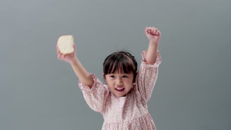 Asiatic-child-eating-piece-of-sweet-in-the-studio-with-a-gray-background