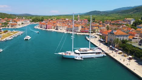 Panorama-of-a-coastal-town-with-many-houses-with-red-roofs,-surrounded-by-the-sea-and-mountains-with-yachts-in-marina-bay-and-Bell-tower-and-walking-peoples