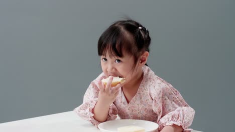 Asiatic-child-eating-piece-of-sweet-in-the-studio-with-a-gray-background