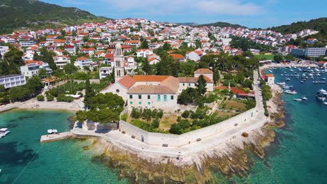 Panorama-of-a-coastal-town-with-many-houses-with-red-roofs,-surrounded-by-the-sea-and-mountains-with-yachts-in-marina-bay-and-Bell-tower