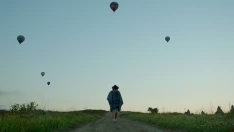 Eine-Gruppe-Von-Heißluftballons-Am-Himmel-Mit-Einer-Frau,-Die-Einen-Weg-Unter-Ihnen-Geht